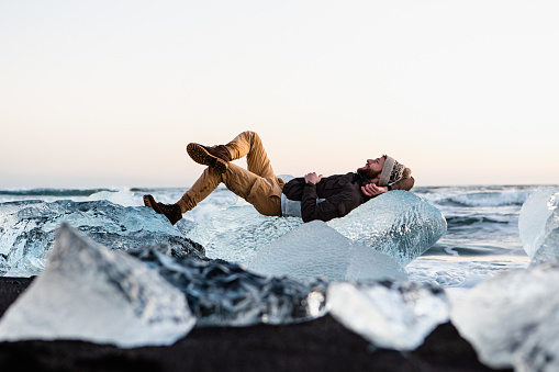 The creative photo of man lying on the crystal ice on the Diamond beach at the sunset in Iceland