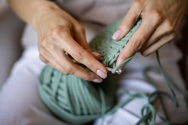 Closeup female hands knitting interior decor basket use green ribbon yarn and crochet needle stock photo