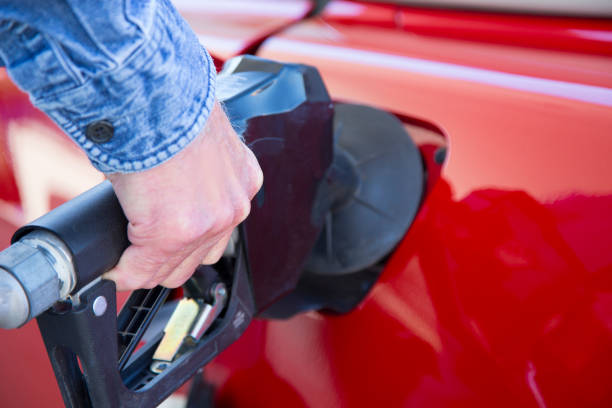 high cost of gasoline due to inflation.  pumping gasoline into vehicle.  red vehicle,  black nozzle. - old men car oil imagens e fotografias de stock