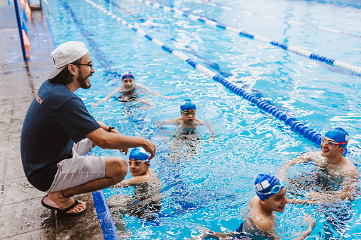 Sports, swimming and coach with a timer for training, exercise or a extreme sport competition. Fitness, pool and athlete or swimmer doing a cardio workout or practice with a mentor with a watch.