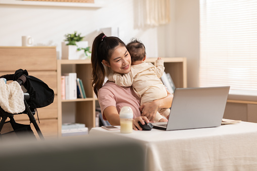 La madre sostiene al bebé mientras trabajaba en la computadora portátil. El bebé de la inocencia apoya su cabeza en su madre y ambos se abrazan. Mamá y su hijo están sentados en la acogedora sala de trabajo. photo