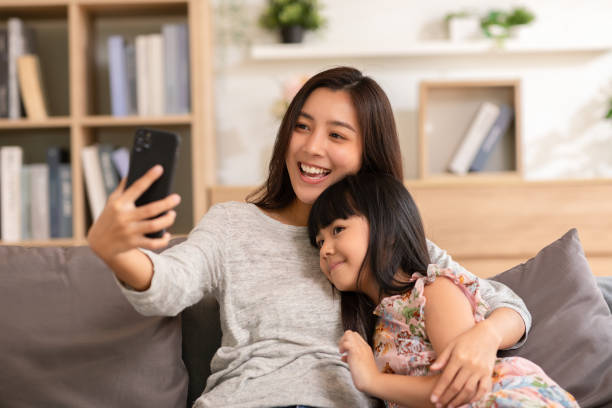 istock Asian mom and her kid are calling on smartphone. Both happy using cellphone for video call smiling mom and girl having fun greetings online with making video call communication through application. 1389415680
