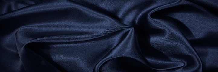 Black blue silk, satin. Shiny fabric surface. Beautiful wavy folds. Dark elegant background with space for design. Web banner.