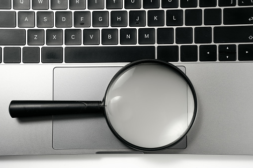 Computer and magnifying glass on white background board