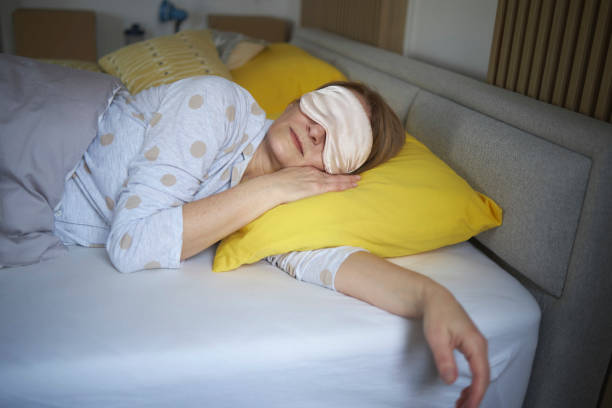 Senior woman sleeping on bed with sleeping eye mask stock photo