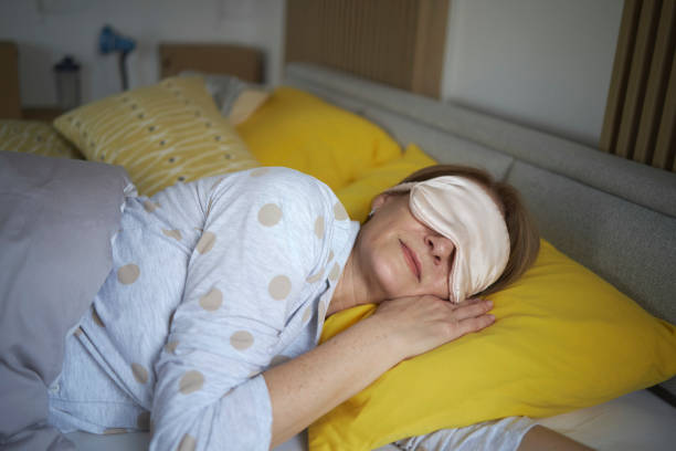 Senior woman sleeping on bed with sleeping eye mask stock photo