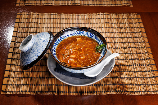Spicey red soup served in traditional ceramic crockery on bamboo place mat on wooden table
