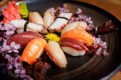 Close-up on various nigiri pieces served with wasabi and ginger on wooden table, decorated with cherry blossom and dandalion