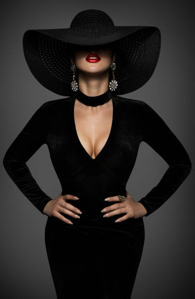 大きな帽子と黒い裂け目のドレスでセクシーなファッションの女性。魅惑的なボディコンガウンの曲線のボディ形状を持つ美しさのモデル。ダークグレーの背景に神秘的なエレガントな女性� - jewelry fashion model women gem ストックフォトと画像