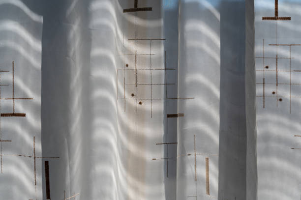 istock Beige tulle hangs against the window. Wavy fabric with brown pattern. Geometric repeating shadows 1389427334