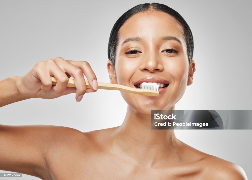 Studio portrait of an attractive young woman brushing her teeth against a grey background Keeping my smile bright and beautiful Bamboo - Material Stock Photo