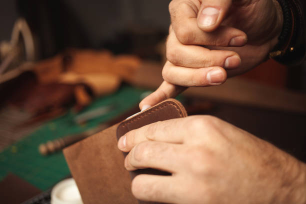 istock tanner makes genuine leather wallet, professional craftsman, closeup, indoor, authentic, business. Handiwork. lubricates edges with cream 1389432499