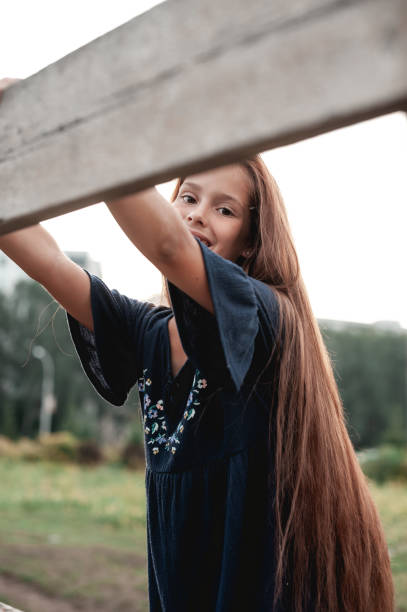 une adolescente mignonne aux cheveux longs a l’air mignonne devant la caméra tenant une planche de clôture en bois avec les deux mains. chercher. pas une scène urbaine. image de stock. - looking at camera one person urban scene photography photos et images de collection