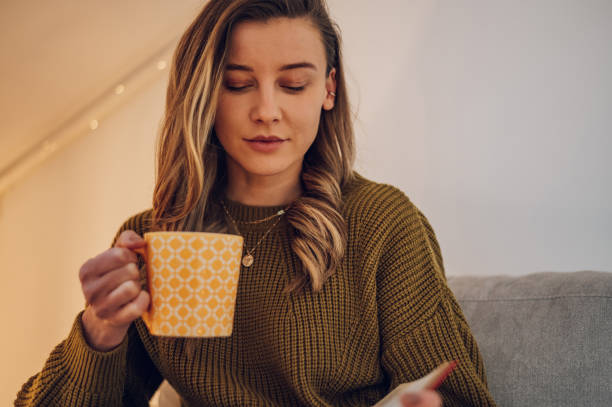 istock Woman reading a book and drinking tea while sitting on the couch at home 1389438778