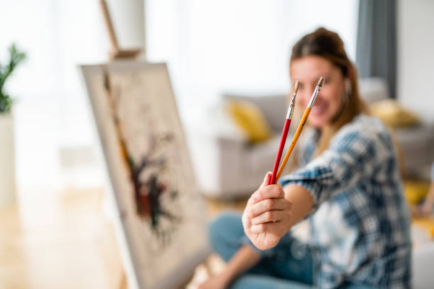 istock Happy young woman paints on canvas at home 1389439556