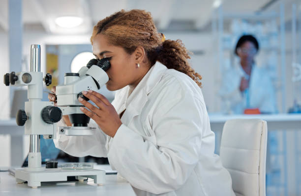 istock Shot of a young female lab worker analysing samples through a microscope 1389440096