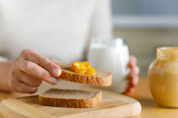 junge frau, die marmelade auf einem toastbrot ausbreitet - toast preserves breakfast bread stock-fotos und bilder