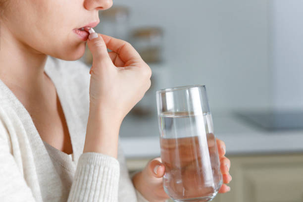 Young woman holding a glass of water and medication in the kitchen stock photo