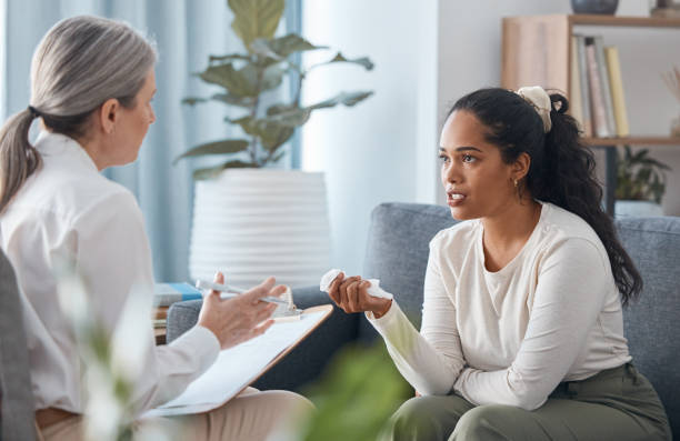 foto de una atractiva joven sentada y hablando con su psicólogo durante una consulta - profesional de salud mental fotografías e imágenes de stock