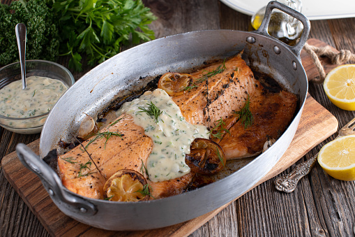 Delicious oven roasted or baked half salmon fillet with homemade tartar sauce. Served in a rustic roasting pan on wooden table from above. Closeup and ready to eat