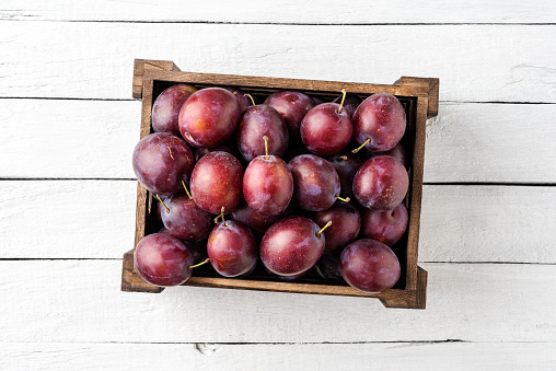 Juicy plums in box on white wooden table. Top view