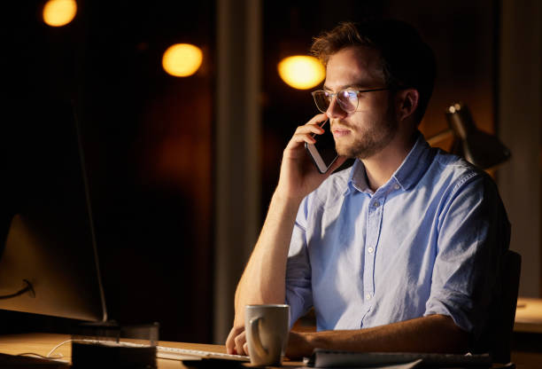 istock Shot of a young businessman talking on a cellphone while working on a computer in an office at night 1389453649
