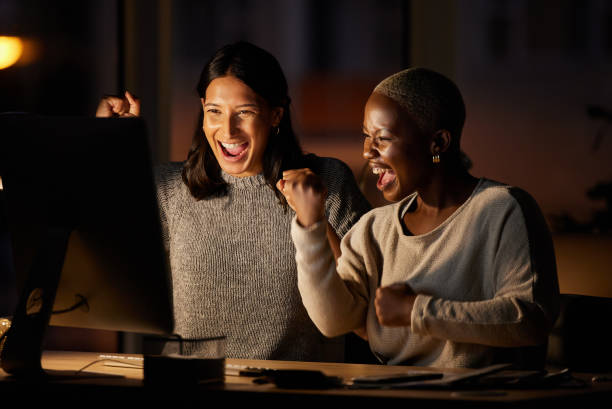 scatto di due donne d'affari che applaudono mentre lavorano insieme su un computer in un ufficio di notte - businesswoman business cheering women foto e immagini stock
