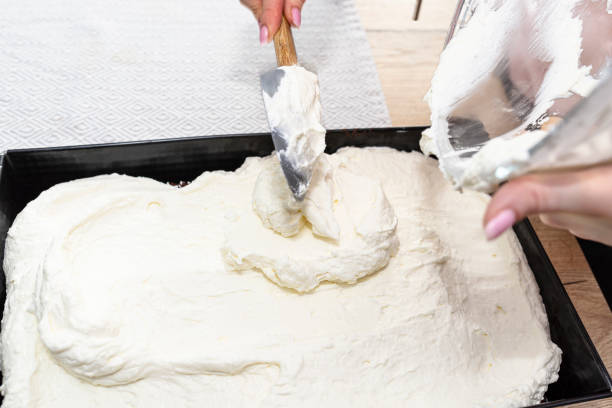ある女性が、ミックスされたカードとホイップクリームをベーキングトレイの中の焼きココアケーキに注ぎます。 - bread bakery women cake ストックフォトと画像