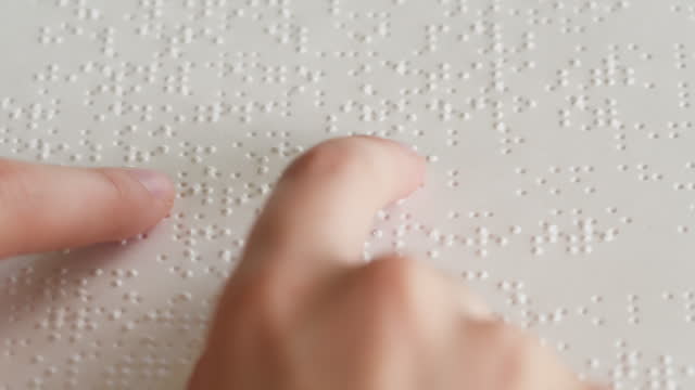 Touching letters on sheet of paper close-up, blindman reading braille book using his fingers, poorly seeing person learning to read, disabled people concept