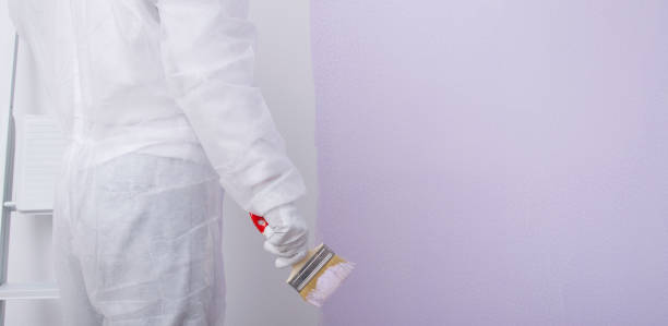istock a builder in protective clothing is going to paint the wall with a brush in a light purple color, there is a place for an inscription 1389458350