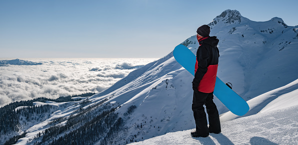 Young active man with snowboard looking at sunset in cloudy mountains