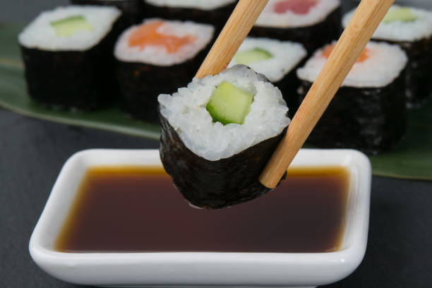 palitos de bambú sumergen un rollo con pepino en salsa de soja - niguiri sushi fotografías e imágenes de stock