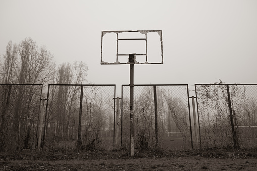Abandoned broken basketball court in the city park. foggy day
