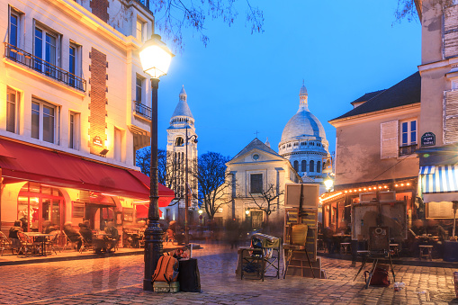 Beautiful urban city life view of Place du Tertre with the Sacre-Coeur Basilica in Paris, France, on a spring evening after sunset in the blue hour