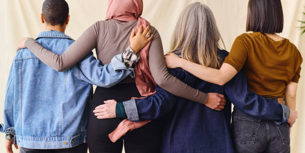 International Women's Day rear view portrait of four women standing with arms around each other in solidarity International Women's Day rear view portrait of four women standing with arms around each other in solidarity powerful women stock pictures, royalty-free photos & images