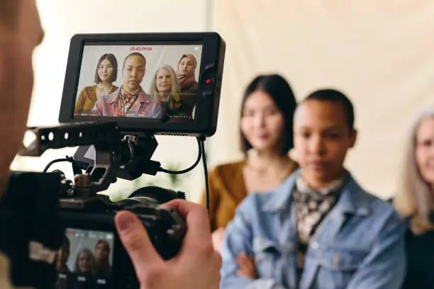Photo of Videographer filming group of multiethnic women for International Women's Day with digital image on camera screen