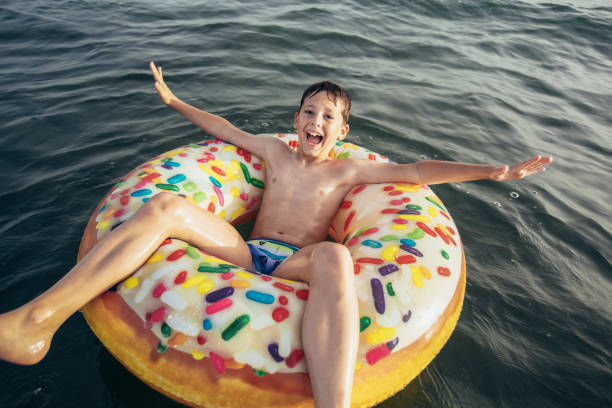Joyful child on inflatable ring ride on breaking wave. Travel lifestyle, swimming activities. Selective focus