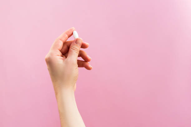 istock Woman holding one white pill on pink background. 1389469292