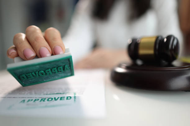 Hand puts stamp approved on document near judge's gavel stock photo