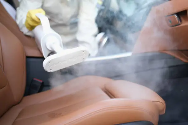 Close-up of a car wash employee cleaning the interior of a car with steam. Dry cleaners, vacuum cleaning