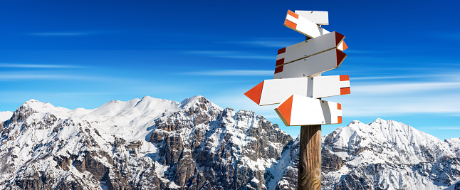 Group of blank directional trail signs with snow capped mountain peaks on background and copy space. Italian Alps, Dolomites, Europe.