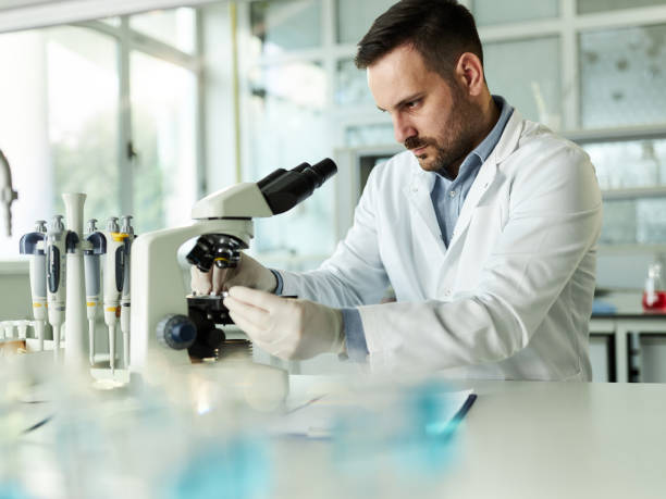 istock Young male chemist adjusting his sample on a microscope in laboratory. 1389472686