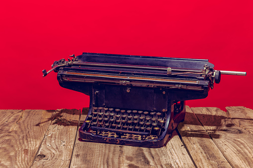 Object. Pop art photography. Retro old, shabby typewriter standing on wooden table isolated on bright red background. Vintage, retro 80s, 70s style. Complementary colors, Copy space for ad, text