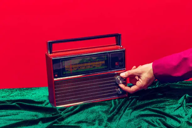 Photo of Retro radio. Female hand touching radioreceiver isolated on red and green background. Vintage, retro fashion style. Pop art photography.