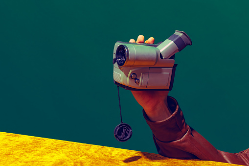 Concept of pop art photography. Using retro gadgets. Human hand holding videocamera isolated on green-yellow background. Vintage, retro 80s, 70s. Complementary colors. Concept of memory, nostalgia