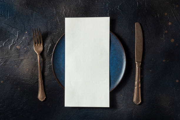 Dinner menu or invitation concept. A fork, a knife, and a blue plate with a card Dinner menu or invitation concept. A fork, a knife, and a blue plate with a white card, overhead flat lay shot on a black background restaurant table card stock pictures, royalty-free photos & images