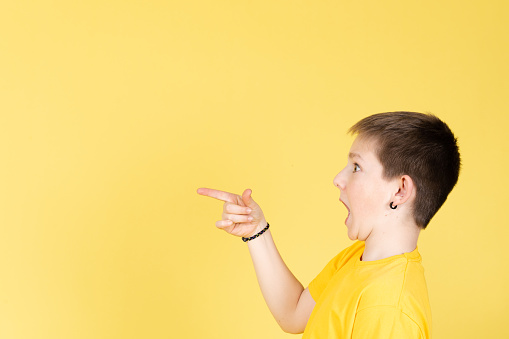 Surprised boy looking and pointing to copy space isolated on yellow background.
