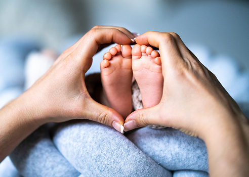 Newborn baby's feet on mother heart shaped hands at home