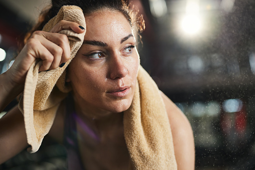 Tired female athlete cleaning sweat with a towel after sports training in a gym.