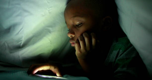 istock Young boy looking at cellphone screen at night under blanket 1389481821